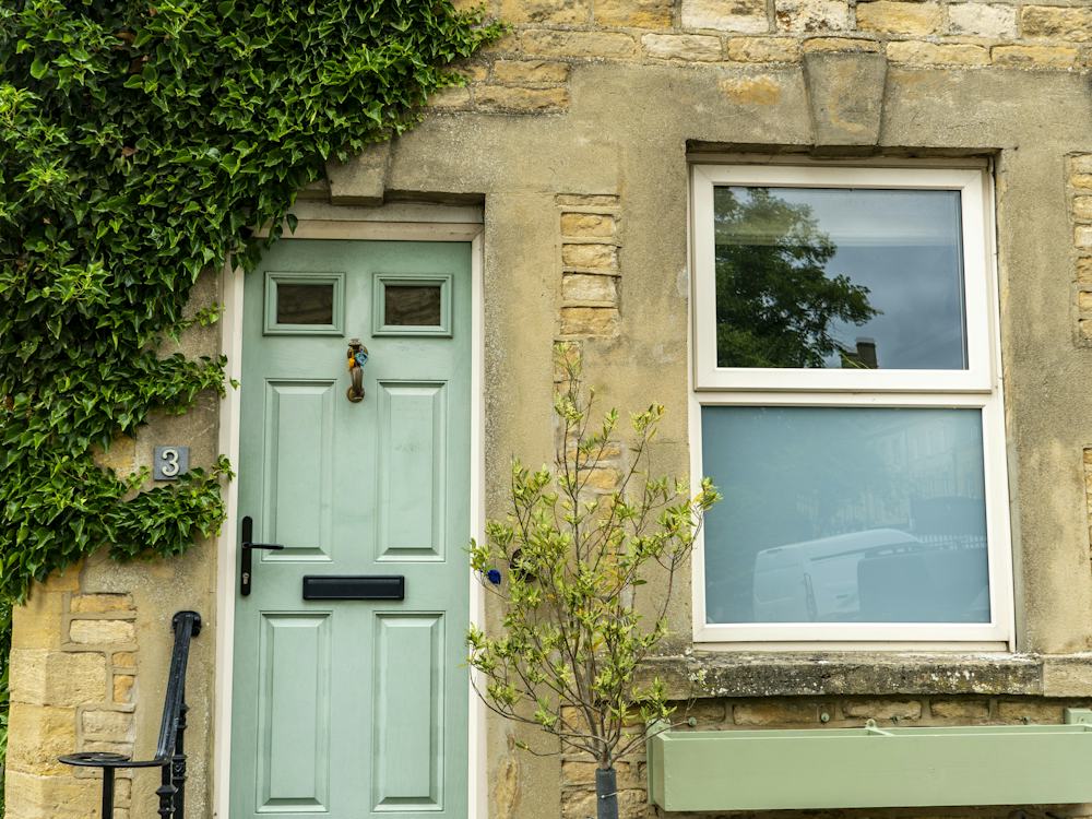 A stone cottage with a green front door and ivy